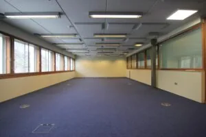 Lege kantoorruimte aan de De Ruijterkade met blauwe vloerbedekking en grote raampartijen.